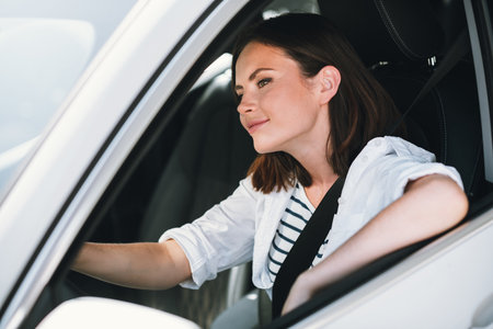 Young woman driving through city streets on a sunny day, enjoying the freedom and adventure of solo...