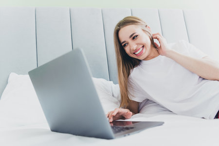 Photo of adorable sweet lady sleepwear smiling having rest bed typing sms modern gadget indoors room home houseの写真素材