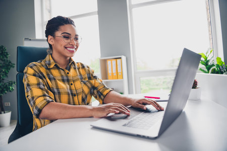 Photo of lovely young lady working netbook dressed yellow plaid shirt comfortable startup office loft room interiorの写真素材