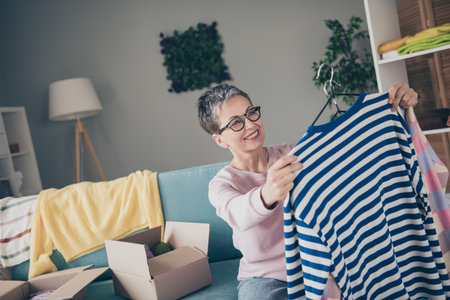 Photo of adorable sweet lady wear pink sweatshirt choosing donation clothes indoors room home house