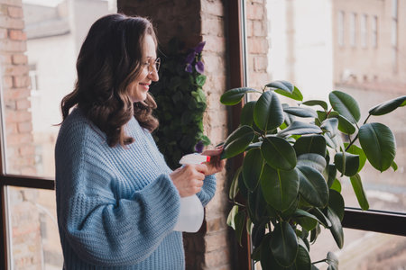 Elderly woman tending to houseplant with smile, enjoying leisure timeの写真素材