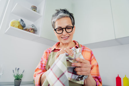 Charming elderly woman enjoying a casual day in her kitchen, preparing with joy.の写真素材