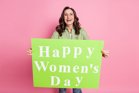Photo of laughing cute senior lady wearing casual outfit holding green placard happy women day isolated on pink color backgroundの写真素材