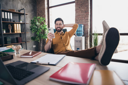 Full length photo of handsome young guy hold device legs table dressed yellow shirt formalwear comfortable startup office room interiorの写真素材