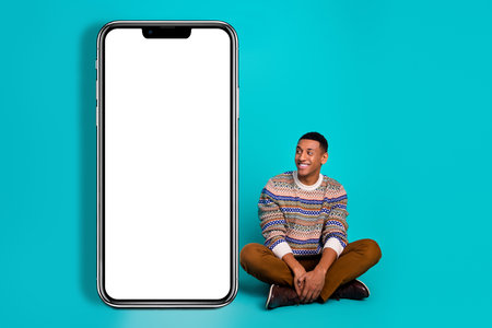 Full body portrait of nice young man look empty space smart phone screen isolated on turquoise color backgroundの写真素材