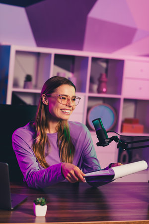 Video chat blogger with glasses hosting a podcast from home office, surrounded by neon lighting, smiling and engagedの写真素材
