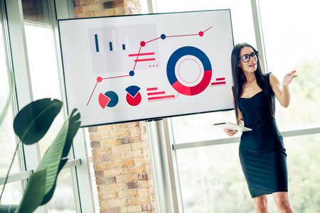 Confident businesswoman presenting data charts in modern office setting, showcasing professional...