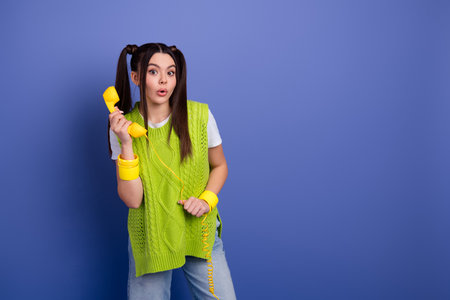 Young woman with bright yellow phone and accessories posing in a blue studio backgroundの写真素材