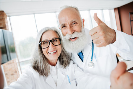 Smiling doctor and friendly physician share a moment with an elderly couple in a bright clinic as they celebrate successful consultation and great health care teamwork for medicine and wellnessの写真素材