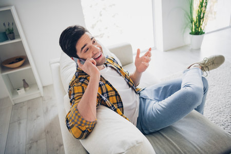 Photo of cheerful positive guy dressed plaid shirt communicating modern gadget enjoying weekend indoors room home houseの写真素材