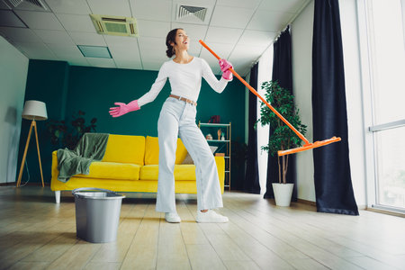 Energetic woman cleans with a mop in a stylish living room with a bright yellow couch and plants creating a lively home sceneの写真素材