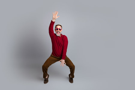 Energetic man in a red sweater posing in a playful stance against a simple gray backgroundの写真素材