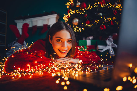 Playful cozy holiday moment a smiling woman in red sweater surrounded by christmas lights gifts and a sparkling treeの写真素材