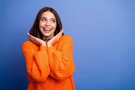 Smiling young woman wearing an orange-knit sweater showing an excited expression on a blue backgroundの写真素材