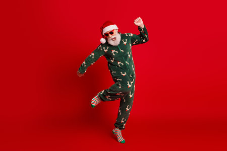 Dancing santa in green reindeer pajama joyful festive vibe against a bold red background perfect Christmas eveの写真素材