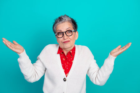 Confident mature woman with short grey hair and glasses wearing a white cardigan and red blouse with arms open against a teal backgroundの写真素材