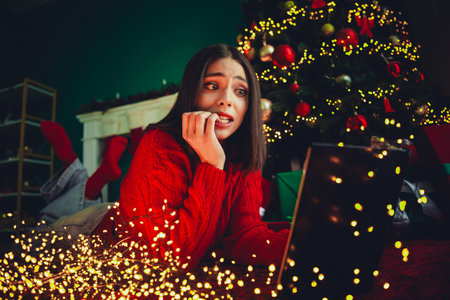 Hectic Christmas moment a woman in a red sweater browses a laptop at home under a twinkling tree and...