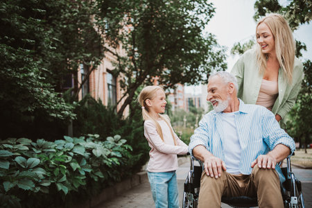 Funny heartwarming family moment in the park with grandpa in wheelchair smiling with daughter and momの写真素材