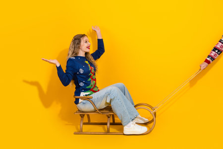 Festive woman enjoying holiday cheer sitting on a sled with a bright yellow backdrop conveying joy and winter celebrationの写真素材