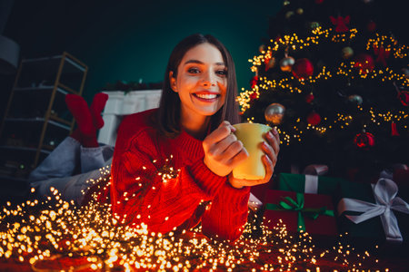 Cozy christmas moment a cheerful woman in red sweater holding mug by twinkling lights and a festive...