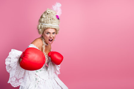 Baroque Style Woman in Elegant Dress with Boxing Gloves Standing Against Pink Background for Creative Fashion Conceptの写真素材