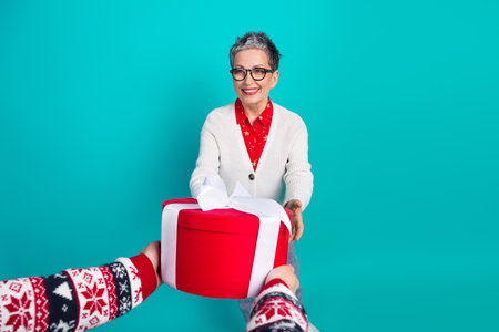A cheerful elderly woman with glasses smiles as she receives a large red gift from a friend against...