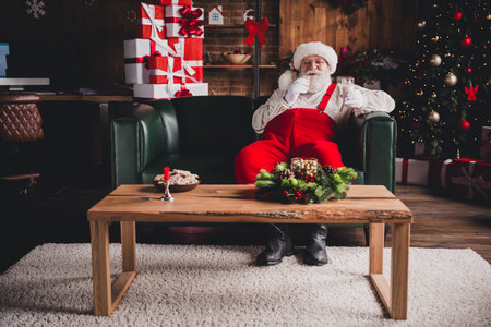 Santa sits comfortably in a cozy living room Christmas tree gifts and warm family holiday scene indoorsの写真素材