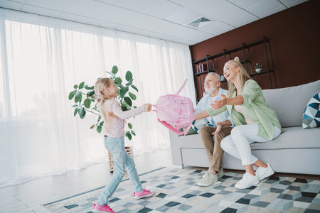 A joyful family moment with a girl returning a pink backpack to her mom and grandpa in a bright cozy living room full of plants and smilesの写真素材