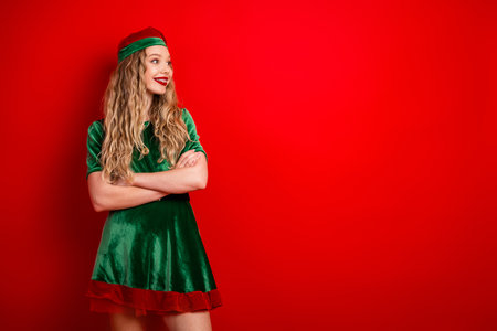 Trendy woman in green elf costume standing with red background celebrating Christmas season and holiday festivities.の写真素材