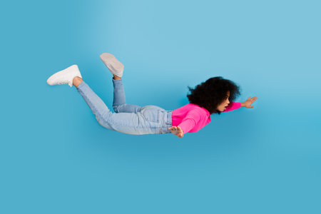 Young woman in stylish outfit floating in air over blue background, promoting casual fashion and showcasing positivityの写真素材