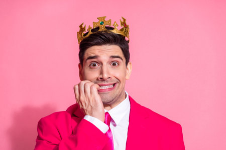 Confident young man wearing a golden crown, posing in a bright pink suit on a vibrant pink background, looking quirkyの写真素材