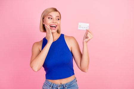 Photo of pretty young woman look debit card empty space wear blue top isolated on pink color...