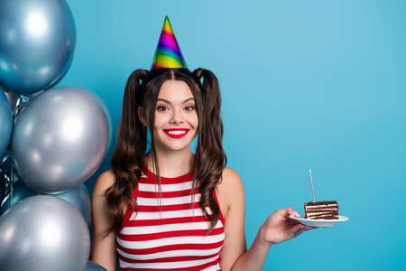 Happy young woman celebrating with birthday cake and balloons wearing colorful party attire on vibrant backgroundの写真素材