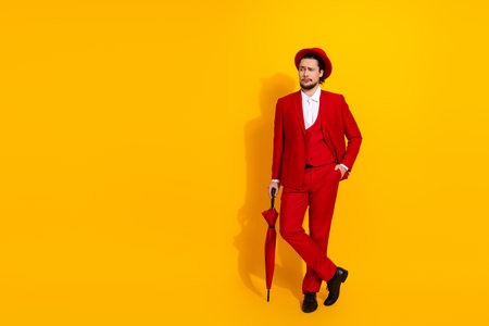 Bold red suited man with umbrella stands against bright yellow background in stylish quirky fashion moment for advertisingの写真素材