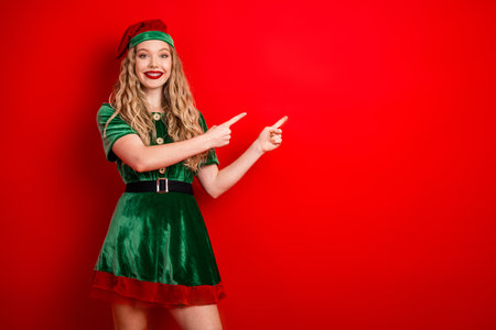 Festive young woman in holiday elf costume gesturing in cheerful excitement against vibrant red...