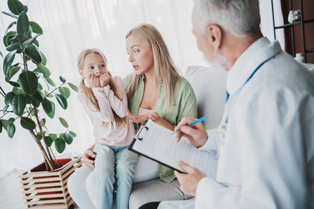 Cheerful family checkup at home a friendly doctor talks to mom and daughter with warm care and smilesの写真素材