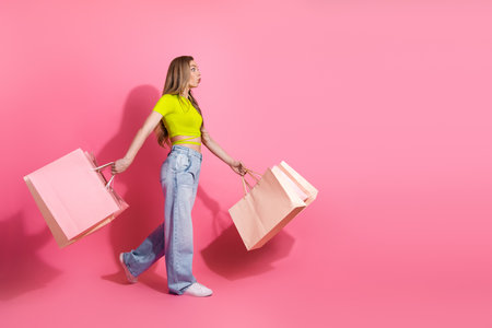 Trendy Young Woman Carrying Shopping Bags on Pink Background Exhibiting Stylish Fashion and Cheerful Lifestyle with Chic Leisure Vibesの写真素材