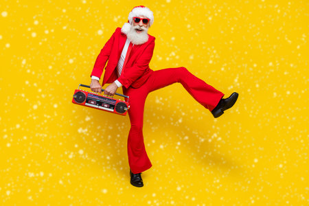 Full length photo of funny positive retired guy wear red tux claus hat dancing enjoying boom box isolated yellow color backgroundの写真素材