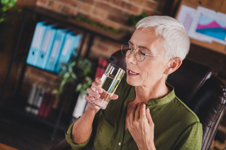 Photo of elderly attractive lady wear shirt drink pills suffer pain workplace workstation loft interior indoorsの写真素材