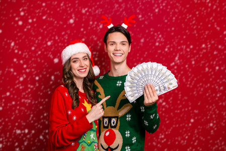 Portrait of two cheerful people indicate finger usd dollar banknotes bills isolated on red color backgroundの写真素材