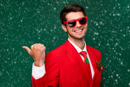 Photo of pretty sweet santa claus guy dressed red jacket glasses pointing back empty space isolated green color backgroundの写真素材