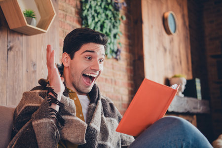 Young man in stylish shirt excitedly reading indoors at comfortable home loftの写真素材