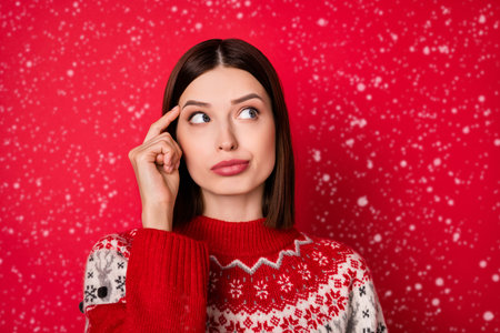 Photo of sweet unsure young woman dressed print pullover finger temple looking empty space isolated red color backgroundの写真素材