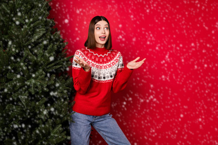 Photo of pretty impressed young lady wear print sweater rising arms looking empty space isolated red color backgroundの写真素材