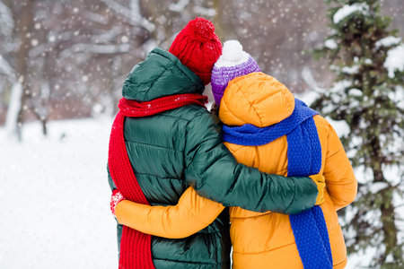 Photo of shiny lovely marriage couple wear windbreakers embracing walking snowy weather outside parkの写真素材