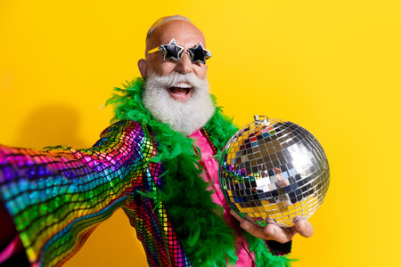 Photo of elderly cool old man take selfie photo discoball wear stylish striped suit boa sunglass isolated on yellow color backgroundの写真素材