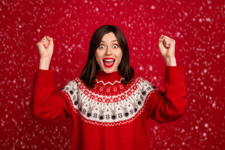 Photo of impressed lucky girl dressed x-mas ornament pullover rising fists screaming isolated red color backgroundの写真素材