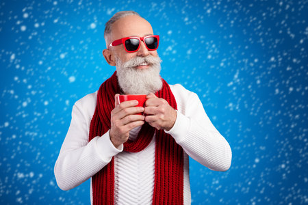 Photo of mature man dressed white pullover red glasses drinking tea looking empty space isolated blue color backgroundの写真素材