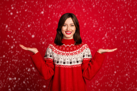 Portrait of positive cheerful cute woman with bob hairdo dressed red sweater hold palms compare products isolated on red color backgroundの写真素材