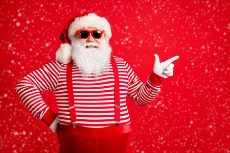 Portrait of a nice, handsome, attractive, cheerful, bearded, gray-haired Santa showing copy space, isolated over a bright red background.の写真素材